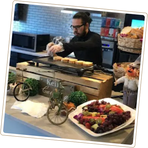 A man with glasses and a bun is cooking on a griddle, while a fruit platter and other decorative items are visible in the foreground.