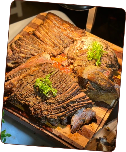 A large, sliced beef brisket with a savory crust, garnished with green onions, resting on a striped wooden cutting board.